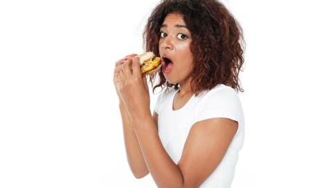 Image of confused young african woman standing isolated over white background. Eating burger.